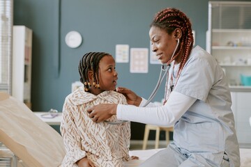 Medical professional with stethoscope examining young patient in brightly lit clinic setting. Child...