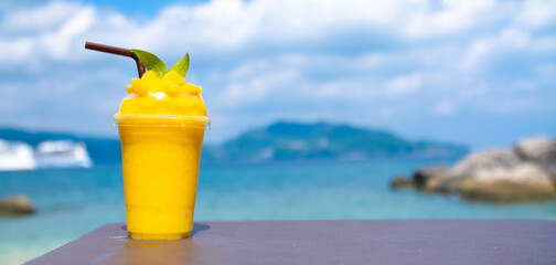 Smoothie made from fresh mango fruits against the backdrop of a seascape. Fruit and yoghurt ice cream decorated with leaves. Glass of tropical dessert close-up.