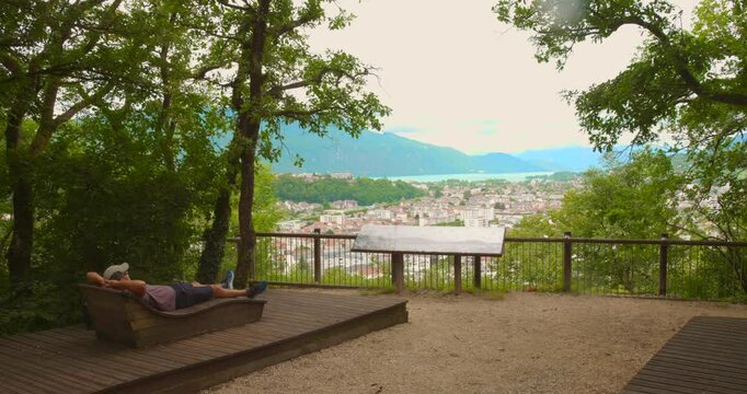 A man rests on a wooden bench at a panoramic viewpoint overlooking Aix Les Bains.