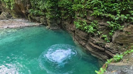 A man cliff jumps from a platform while canyoneering at Kawasan Falls in Cebu, Philippines. He runs and jumps from the platform down into the bright blue water below.