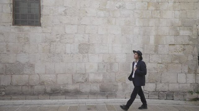 Orthodox Jewish male walks past old wall with book in the old city, Jerusalem