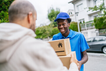 Smiling delivery worker hands a package to customer on a residential street.