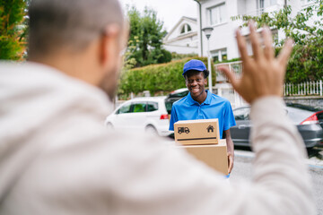 Customer waves goodbye to delivery worker holding packages on a suburban street.