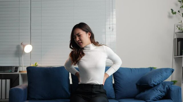 Beautiful woman with charm who is irritated and has back pain, stomachache, feeling unwell, coughing, sitting, lying on the sofa in the living room, need treatment and rest. Concept of body ailment.