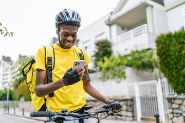 Smiling African delivery cyclist checking his phone during a food delivery shift