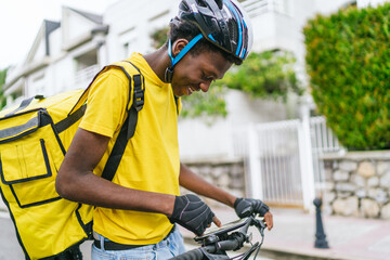 African delivery cyclist checks his GPS on bike in a quiet suburban neighborhood