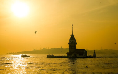 Sunset view of the Maiden's Tower surrounded by water of Bosphorus strait in Istanbul, Turkey on a serene evening.  The tower stands out against the vibrant sunset sky, casting a reflection.