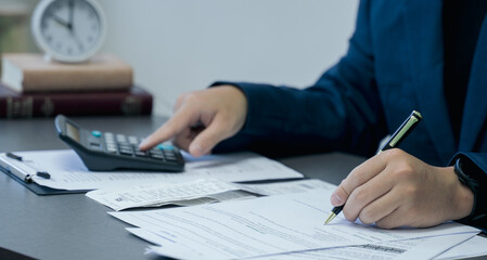 Businessman calculates taxes using calculator and pen to writing note.