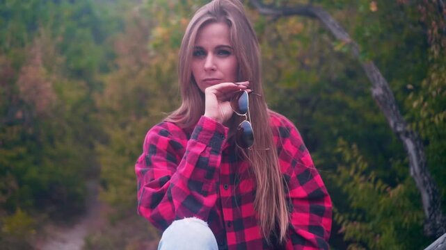 Sexy girl with long hair sits on a dry log against the background of the forest