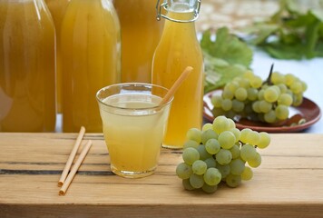 Fototapeta premium Homemade white grape syrup in bottles and grape juice in a glass. Made from fresh aromatic organic white grapes and honey or sugar.