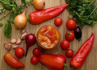 Homemade canned tomato and pepper salsa. Fresh vegetable and spices around - garlic, onion, basil, red peppers and different kinds of tomatoes.