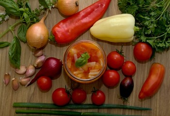 Homemade canned tomato and pepper salsa. Fresh vegetable and spices around - garlic, onion, basil, red peppers and different kinds of tomatoes.