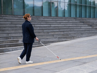 Blind businesswoman walking along tactile tiles with a cane. 