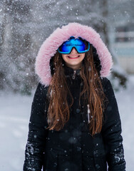 A girl standing outdoors with snow falling around them, wearing a black jacke