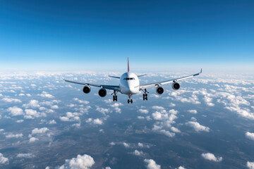 Large commercial airplane flying above the clouds on a clear blue day