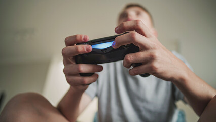 Close up Caucasian teenage boy holding wireless controller in hands while playing online video game on console, sitting on sofa. Teenager spending leisure time at home. Lifestyle concept. Low angle.