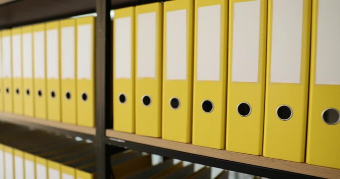 Yellow identical folders with materials and documents are arranged in rows on shelves. Storage of business documents