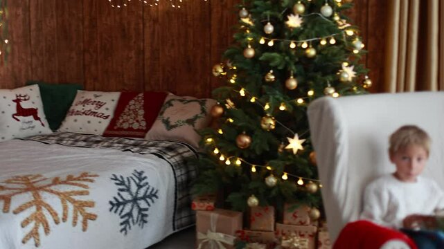 Cute blond child, boy, celebrating Christmas at home, decorated room for the holidays, child reading book and playing
