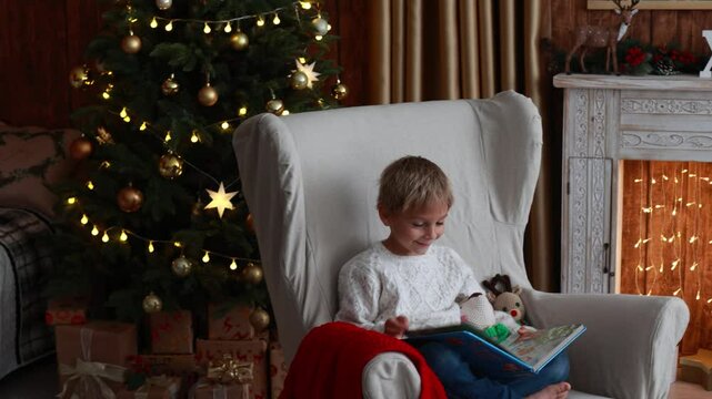 Cute blond child, boy, celebrating Christmas at home, decorated room for the holidays, child reading book and playing