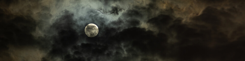 full moon slightly hidden in dramatic night sky with overcast clouds fantasy widescreen panoramic...