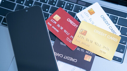 A collection of credit cards in different colors, on a laptop keyboard next to a smartphone. the...