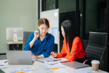 ￼￼Two young Asian professionals engaged in teamwork and business discussions in modern office