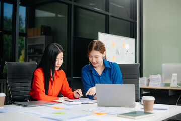 ￼￼Two young Asian professionals engaged in teamwork and business discussions in modern office