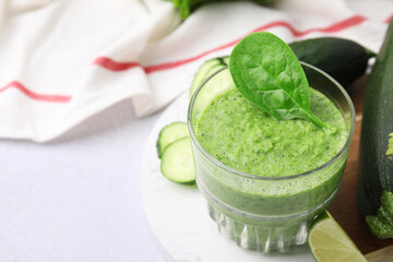 Tasty green smoothie in glass, lime and vegetables on light table, closeup. Space for text