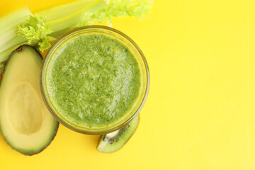 Delicious green smoothie and ingredients on yellow table, top view. Space for text