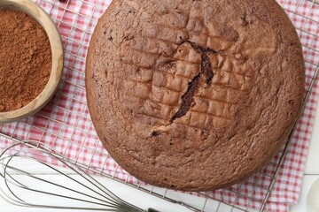 Tasty chocolate sponge cake, whisk and cocoa powder on white wooden table, top view