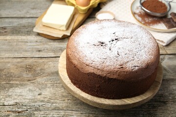 Tasty chocolate sponge cake with powdered sugar and ingredients on wooden table, closeup