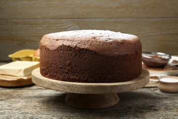 Tasty chocolate sponge cake with powdered sugar and ingredients on wooden table, closeup