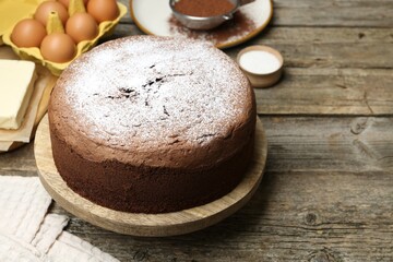 Tasty chocolate sponge cake with powdered sugar and ingredients on wooden table, closeup