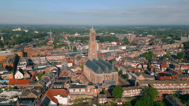 Aerial footage showcasing the city center of Weert, Netherlands with orbit around historic Martinus church tower on a clear summer day, providing panoramic view of the city's layout and architecture. - Powered by Adobe