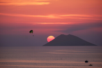 Stromboli volcano island profile with sun in the background.