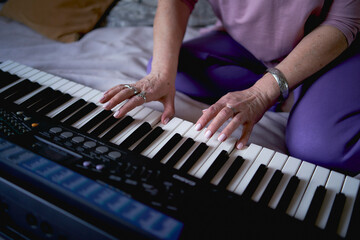Obraz premium A 60-year-old mother and a 40-year-old daughter play the keyboard together on the bed at home