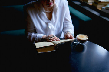Fototapeta premium an elderly woman reads a book in a cafe and drink coffee
