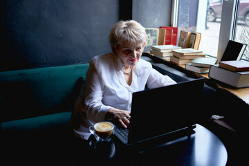 an elderly woman works in a cafe at a laptop