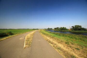 Paved path beside river through rural landscape with clear sky and green fields in Germany