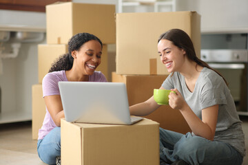 Happy roommates drinking and checking laptop moving home