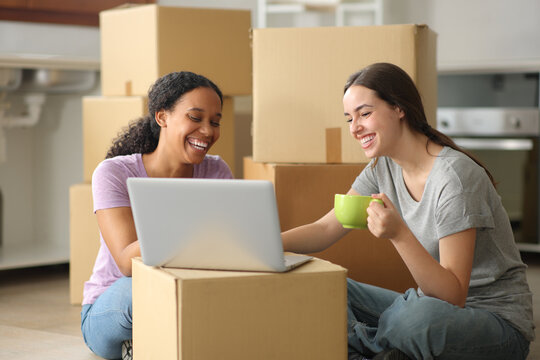 Happy roommates drinking and checking laptop moving home