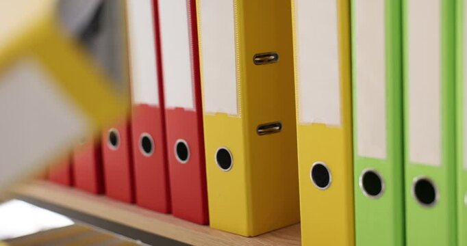 Woman selects folder with documents in row of folders with files and paper. Managed by a system on office shelves