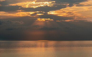 Sun shining through clouds over calm ocean at sunrise