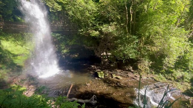Glencar Waterfall in Leitrim, Ireland with a rainbow mist, surrounded by lush greenery and rocky pool.