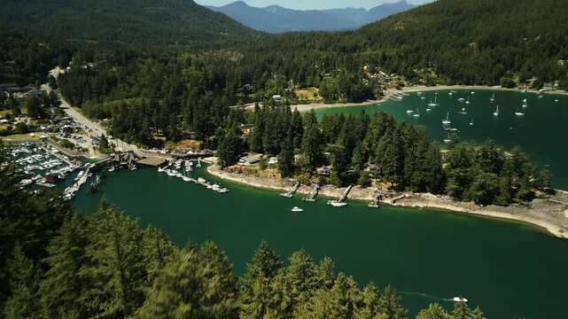 Drone flying over hilltop forest of trees to reveal a tropical and peaceful bay in Bowen Island with lots of boats anchored in the tropical blue water
