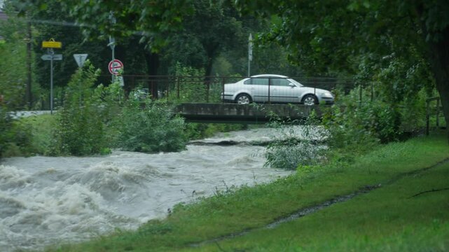 Car crossing the bridge over strong current of river and strangers watching