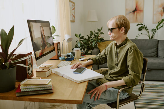 Caucasian man wearing sunglasses sitting at wooden table while listening to audio at home