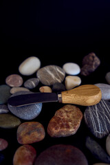Naklejka premium fish and cheese knife with a wooden handle on a black background with sea pebbles