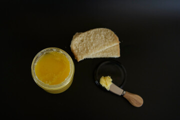 butter ghee in a transparent jar with homemade bread on a black background