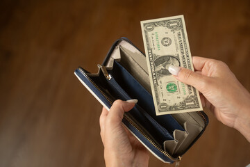 Woman opens a stylish wallet, retrieving a single one dollar bill. The scene captures her hands as she interacts with the cash, highlighting themes of finance and consumerism